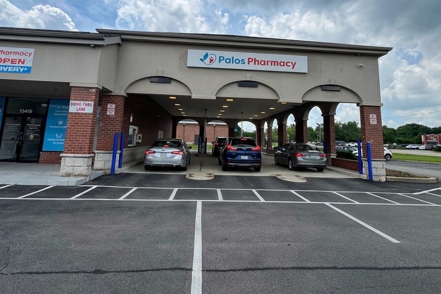 The real Palos Pharmacy storefront in Palos Heights with cars picking up prescriptions in the three covered drive-through lanes